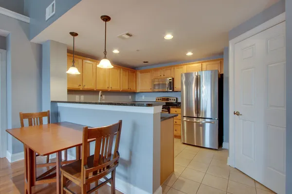 a kitchen with stainless steel appliances granite countertop a refrigerator a sink a stove a dining table and chairs