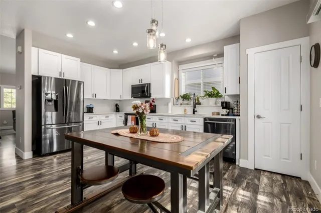 a kitchen with a refrigerator a stove a sink and a dining table with wooden floor