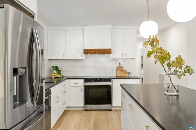 a kitchen with stainless steel appliances granite countertop a refrigerator a sink dishwasher a stove and white cabinets with wooden floor