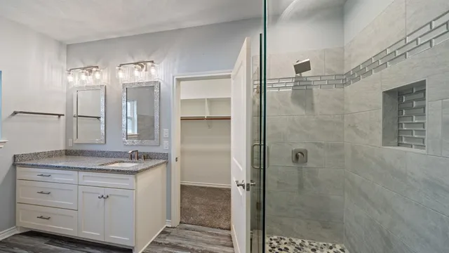 a bathroom with a granite countertop sink two mirror and shower