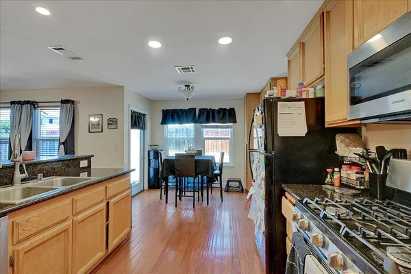 a kitchen with stainless steel appliances granite countertop a stove top oven a sink a dining table and chairs with wooden floor
