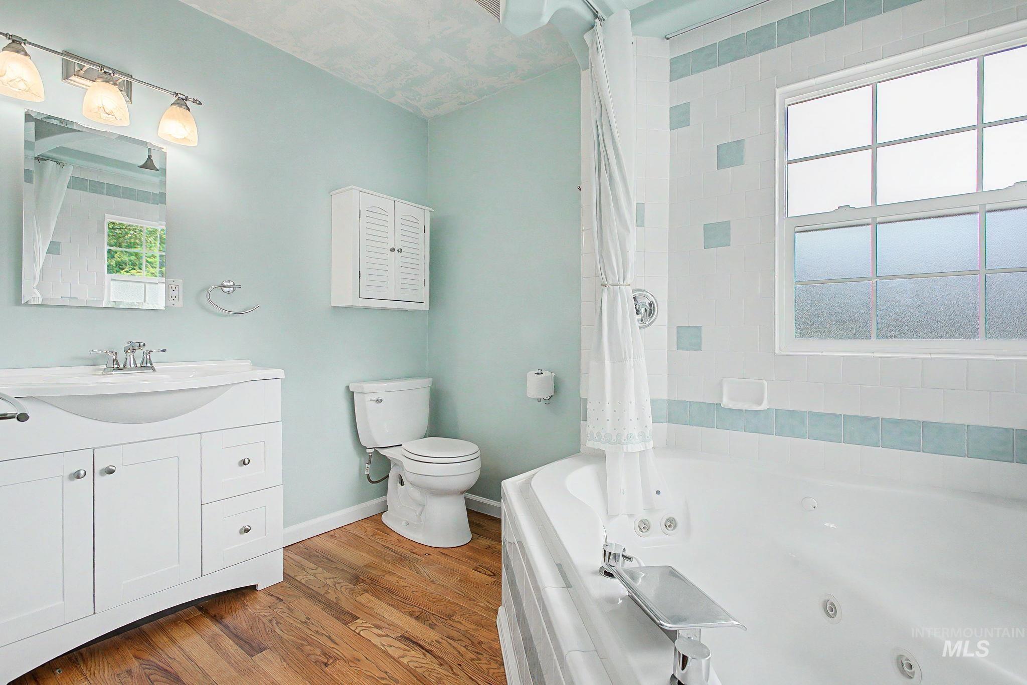 3314 6th Street Lewiston, ID 83501 - Photo 23 of 50 Bathroom featuring a white vanity with integrated sink, wood-finish flooring, a jetted bathtub with white and accent tile surround, and a window providing natural light