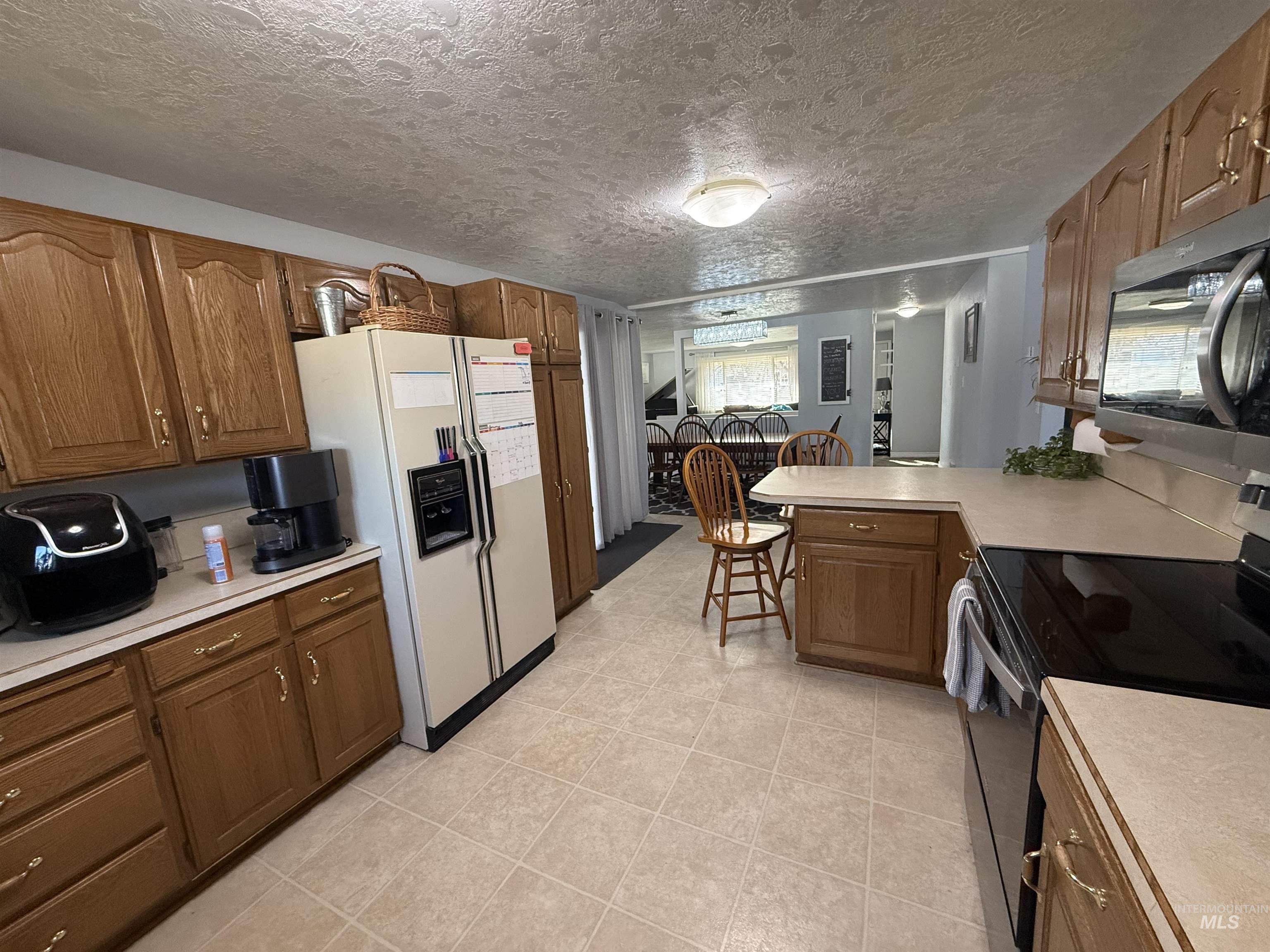 4926 Easy Street Chubbuck, ID 83202 - Photo 20 of 29 Kitchen with electric range oven, light countertops, a peninsula, white refrigerator with ice dispenser, and a textured ceiling