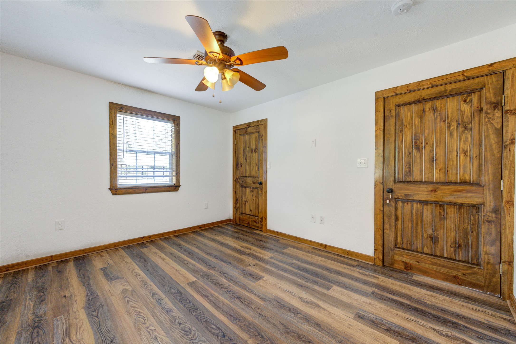 8805 Sun Oil Road Brenham, TX 77833 - Photo 29 of 50 Bright and inviting room featuring rich wood floors, a ceiling fan, and rustic wooden accents on the doors and window frame.
