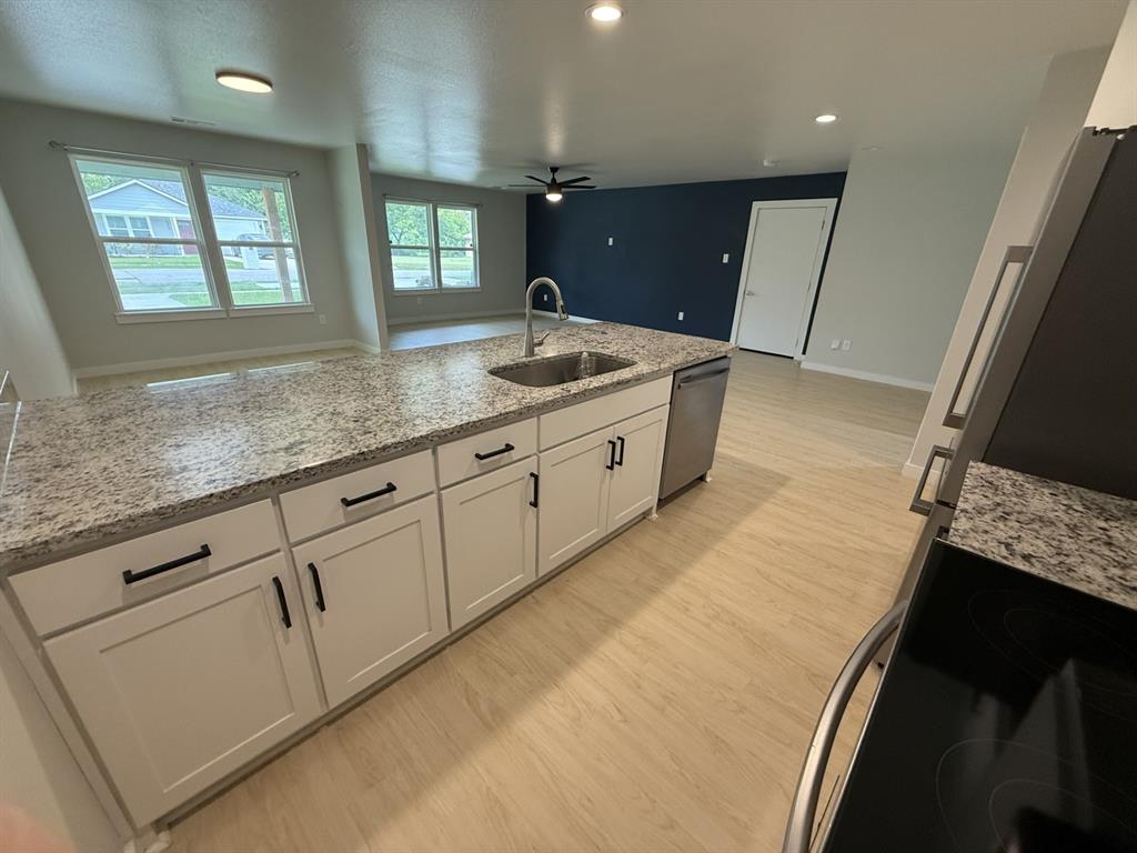 505 Thomas Street Terrell, TX 75160 - Photo 6 of 38 Kitchen island featuring a stainless steel sink with a high-arc faucet, granite-finish countertop, and white shaker-style cabinetry with matte black hardware