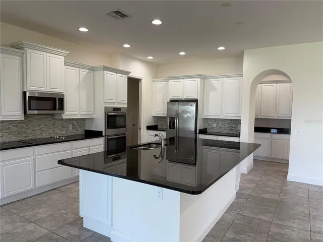 a large kitchen with granite countertop a sink and white cabinets