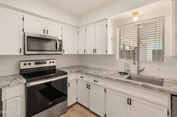 a kitchen with granite countertop a sink cabinets stainless steel appliances and a window