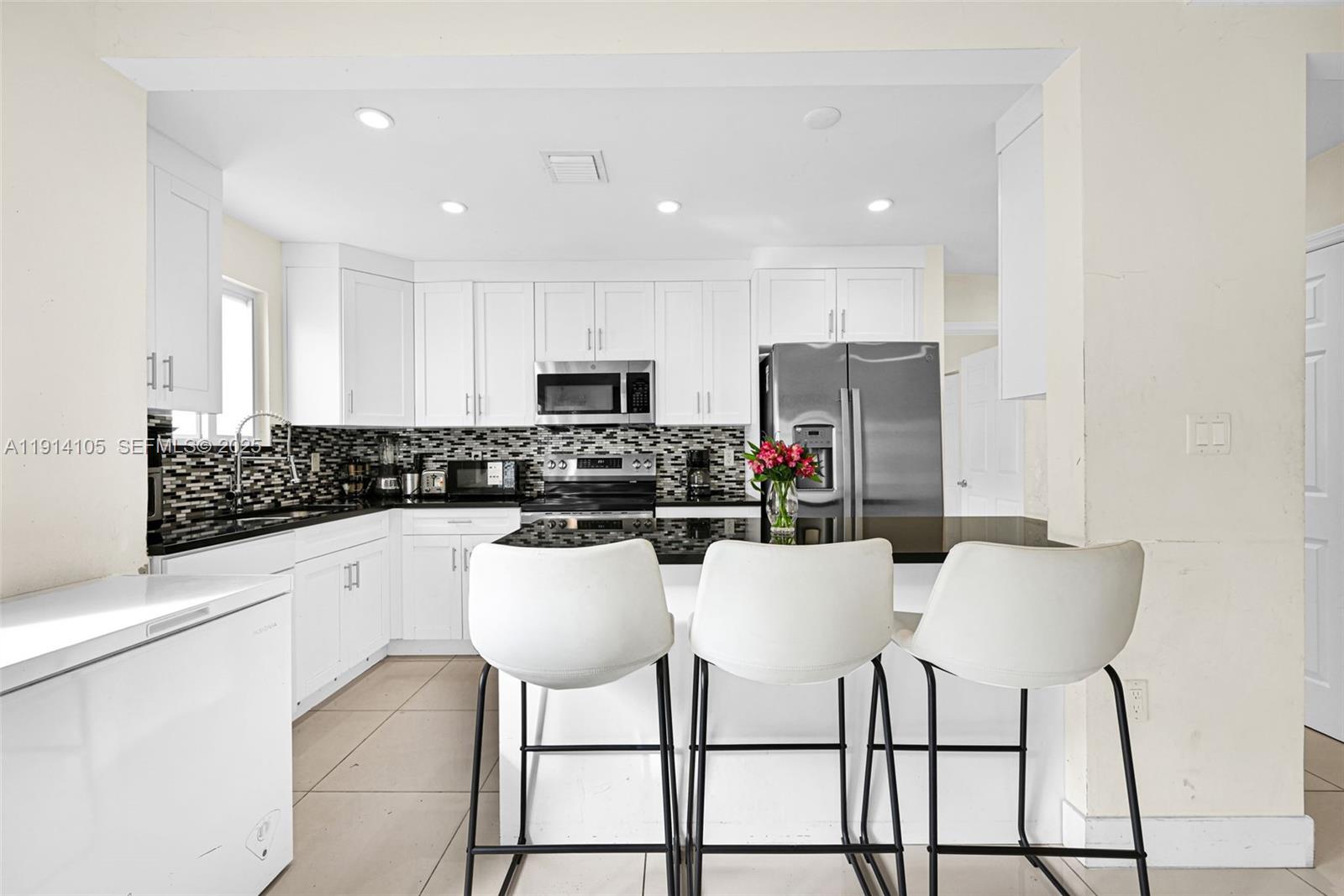 26100 Southwest 134th Place Homestead, FL 33032 - Photo 9 of 39 a kitchen with kitchen island granite countertop a dining table chairs refrigerator and microwave