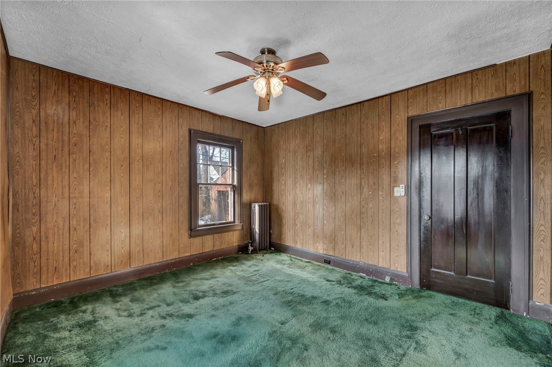 3272 Tullamore Road Cleveland, OH 44118 - Photo 39 of 47 Carpeted empty room with radiator heating unit, a ceiling fan, wooden walls, and a textured ceiling
