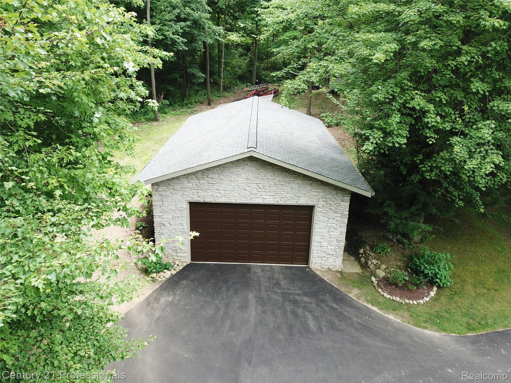9867 Rainbow Ridge Drive Schoolcraft, MI 49087 - Photo 6 of 82 Stone veneer garage with a dark brown overhead door, asphalt driveway, gray shingle roof, and surrounding mature trees