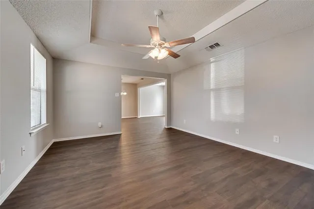 an empty room with wooden floor chandelier fan and windows