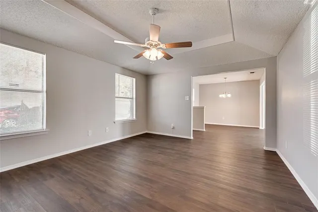 an empty room with wooden floor chandelier fan and windows