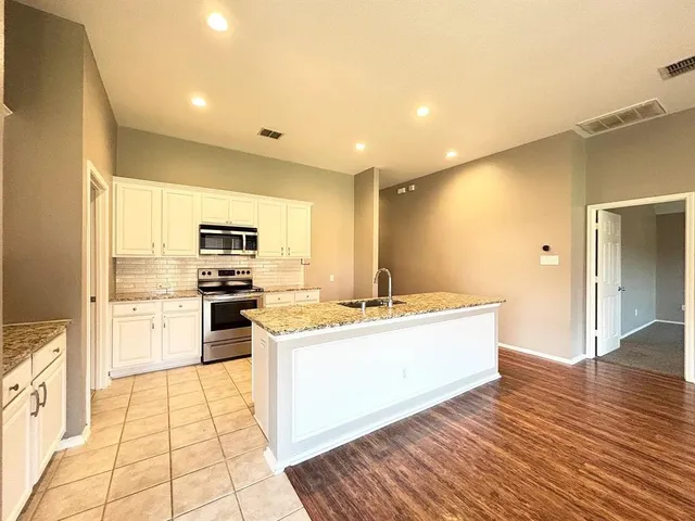 a large kitchen with a stove a sink dishwasher a refrigerator and white cabinets with wooden floor