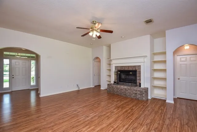 an empty room with wooden floor a chandelier fan and a fireplace