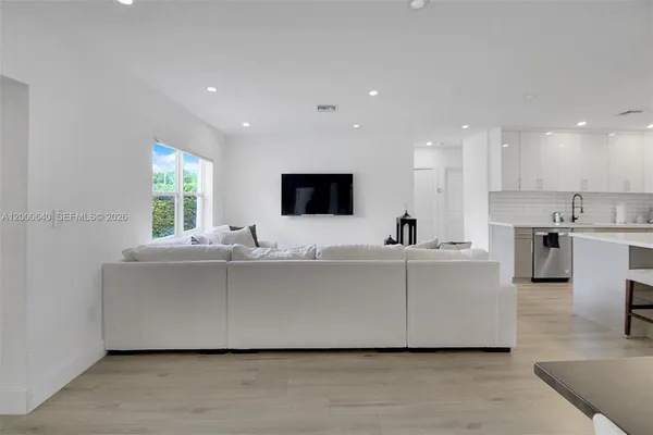 a living room with stainless steel appliances kitchen island a sink a flat screen tv and windows