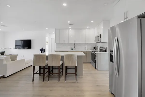 a kitchen with stainless steel appliances granite countertop a dining table chairs refrigerator and sink