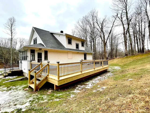 a view of a white house with a big yard plants and large tree
