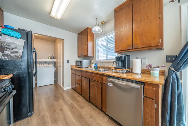 a kitchen with stainless steel appliances granite countertop a refrigerator a sink dishwasher a stove and white countertops with wooden floor