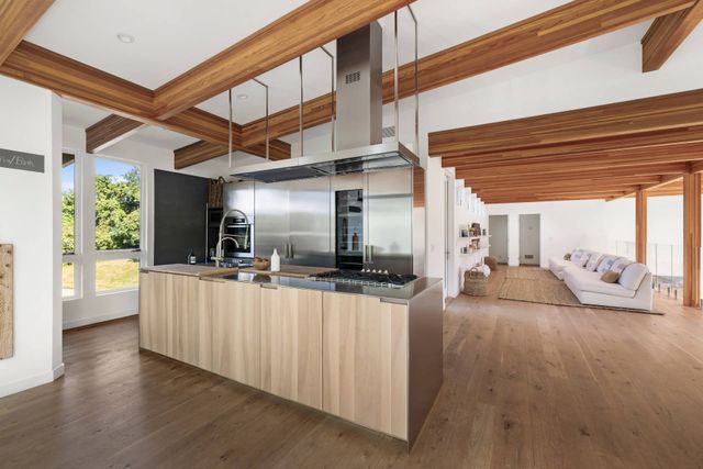 a large white kitchen with kitchen island granite countertop a large window a sink and stainless steel appliances