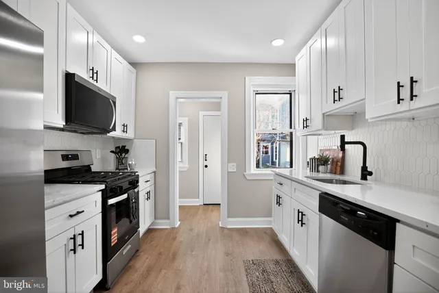 a kitchen with stainless steel appliances granite countertop a stove top oven a sink dishwasher and a refrigerator with wooden floor