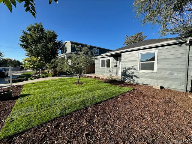 a view of a white house with a big yard plants and large trees