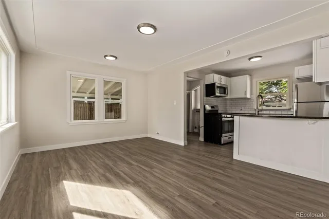 an empty room with wooden floor and a kitchen
