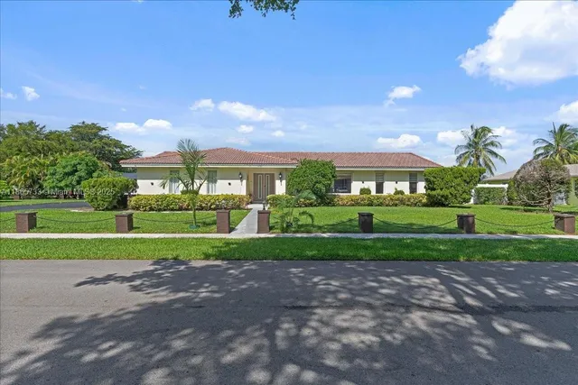 a view of a big house in front of a big yard with plants and large trees