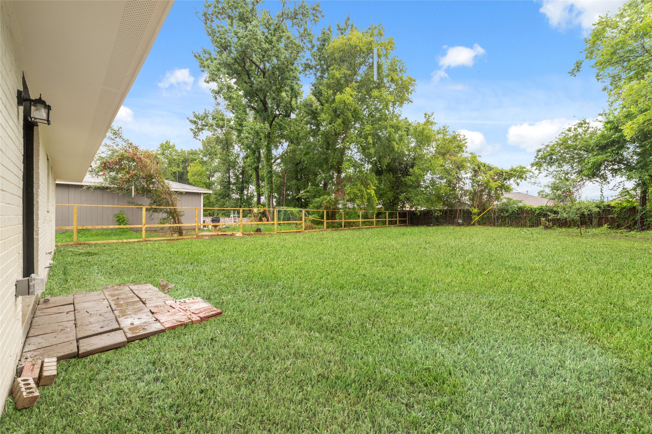 5709 Langley Road Houston, TX 77016 - Photo 24 of 27 Spacious backyard with lush green grass, bordered by trees and a wooden fence, perfect for outdoor activities and relaxation.