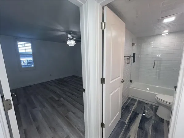 an empty room with wooden floor chandelier fan and windows
