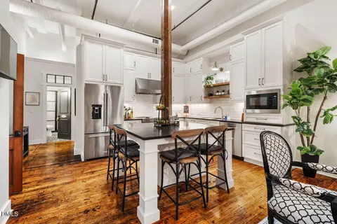 a kitchen with stainless steel appliances kitchen island granite countertop a dining table chairs and a refrigerator