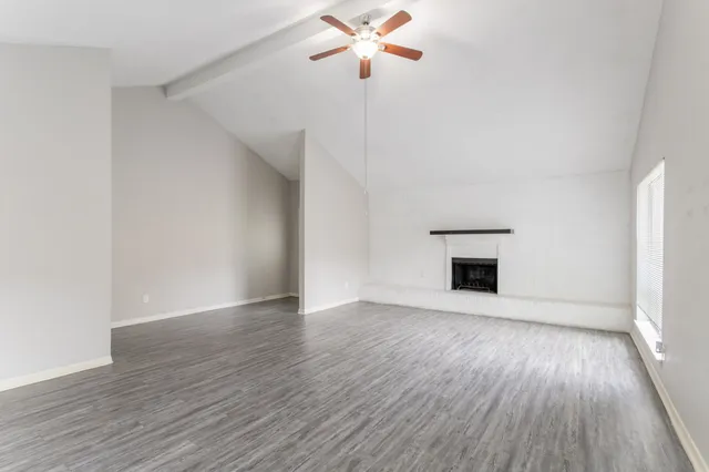 an empty room with wooden floor chandelier fan and windows