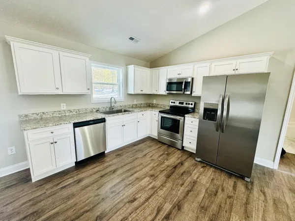 a kitchen with granite countertop a refrigerator sink and white cabinets