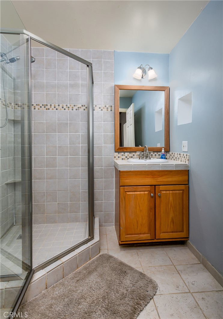 10960 Steinhoff Road Frazier Park, CA 93225 - Photo 45 of 46 A full 4th bathroom located in the private downstairs suite. This space offers an oak vanity with storage, a large mirror with classic lighting, light blue walls, and a convenient glass-enclosed walk-in shower accented with a mosaic tile border.