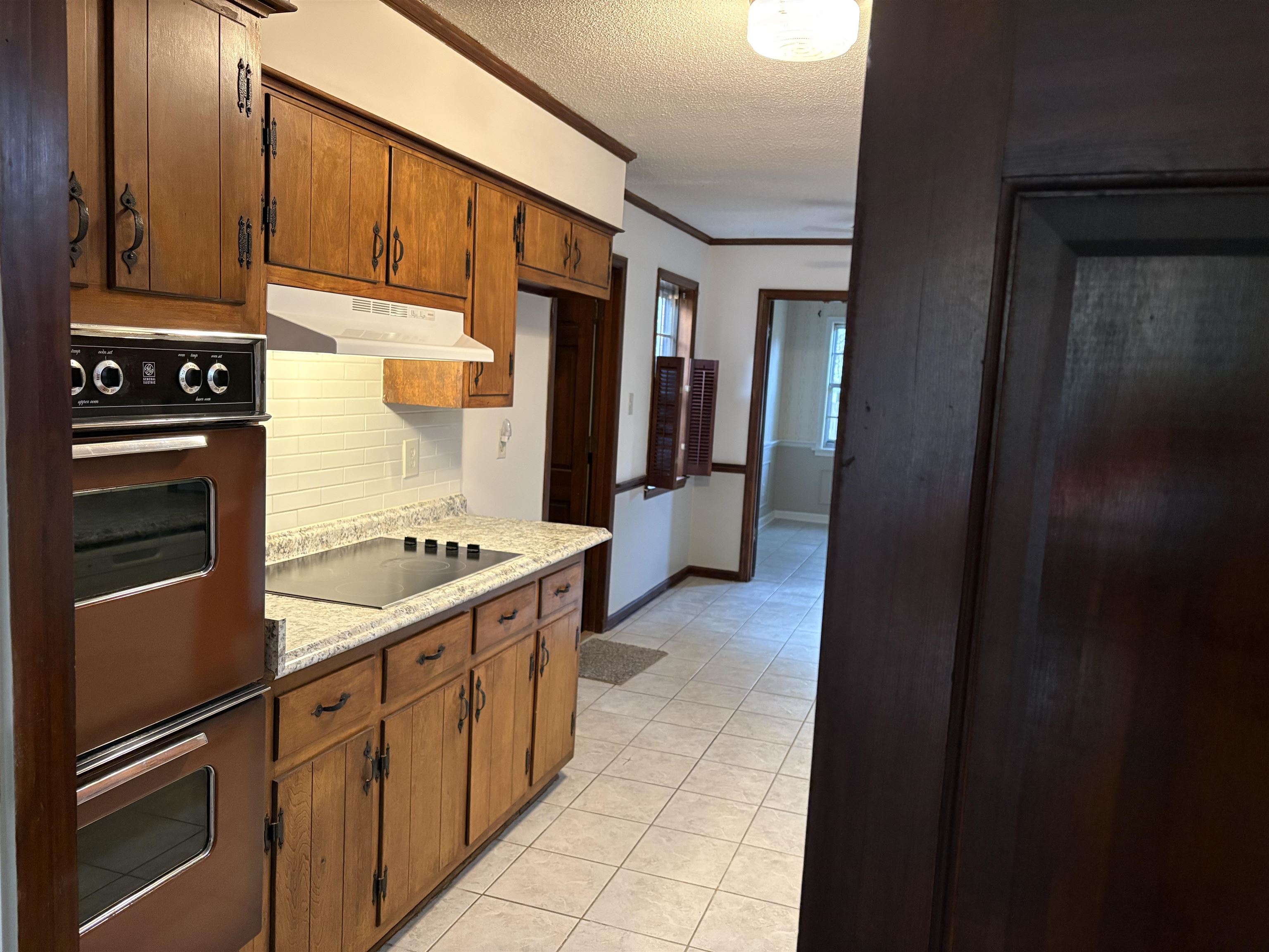 5459 Knight Arnold Road Memphis, TN 38115 - Photo 14 of 38 Kitchen with crown molding, a textured ceiling, light tile patterned floors, black electric cooktop, and backsplash