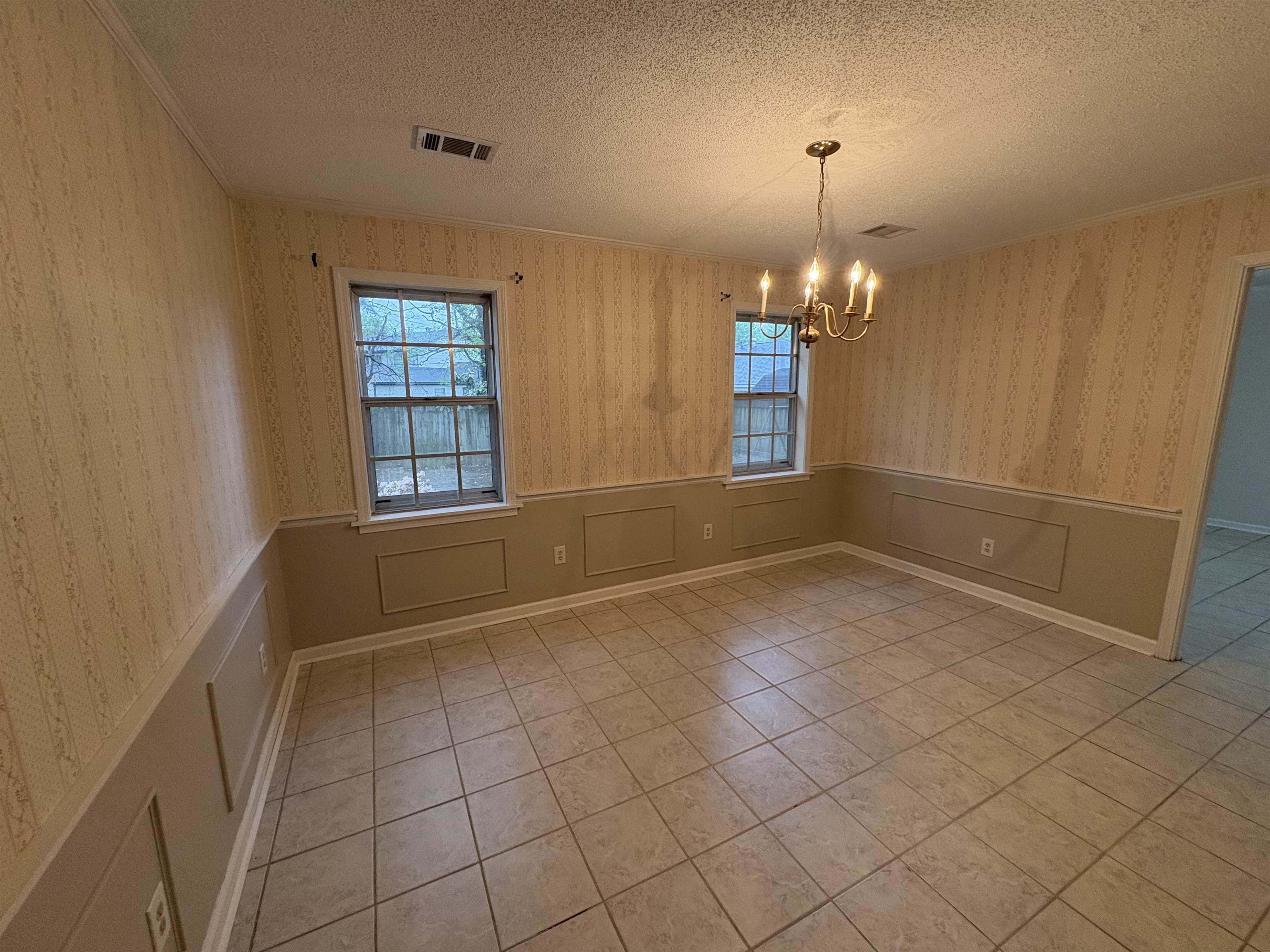 5459 Knight Arnold Road Memphis, TN 38115 - Photo 17 of 38 Unfurnished dining area with a wainscoted wall, wallpapered walls, a textured ceiling, ornamental molding, and suspended lighting