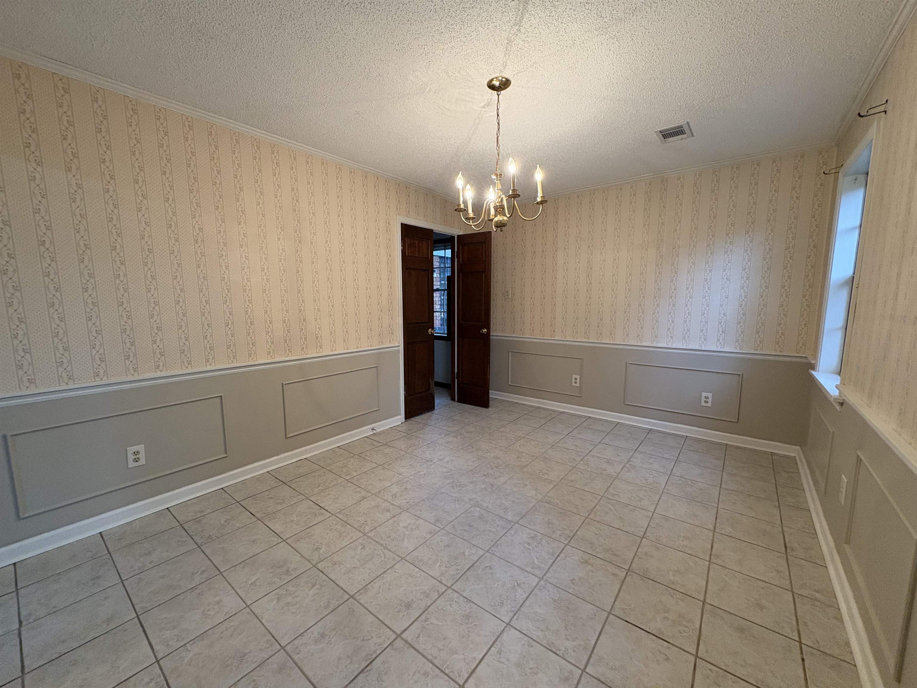 5459 Knight Arnold Road Memphis, TN 38115 - Photo 18 of 38 Unfurnished dining area with a textured ceiling, a wainscoted wall, suspended lighting, light tile patterned flooring, and ornamental molding