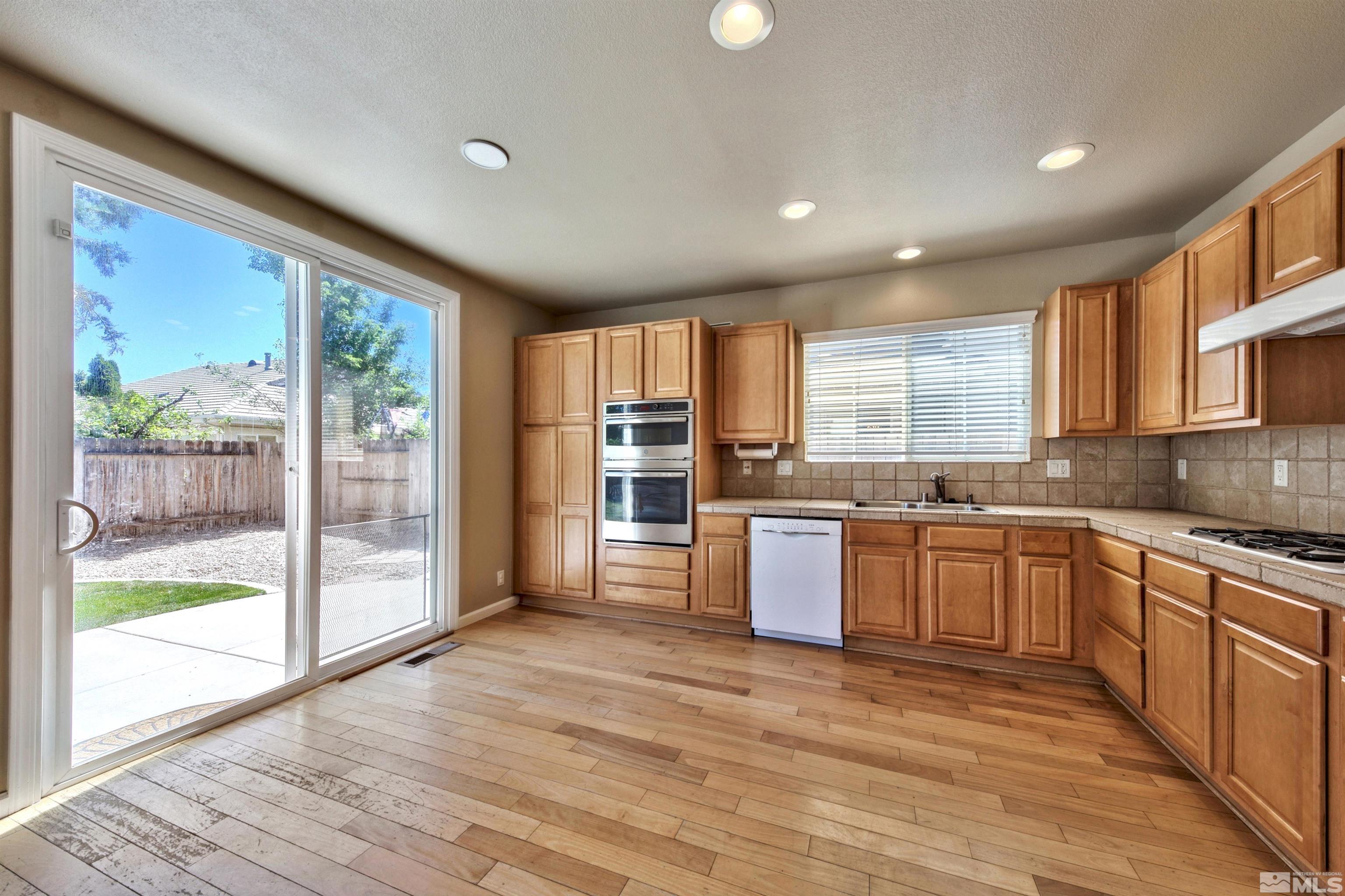 10084 Silver Star Drive Reno, NV 89521 - Photo 4 of 26 a large kitchen with stainless steel appliances granite countertop a refrigerator a sink dishwasher a stove and a large window with wooden floor