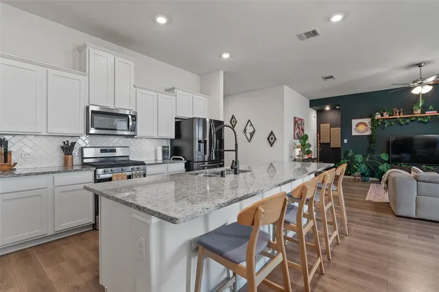 a kitchen with stainless steel appliances granite countertop a stove top oven a refrigerator a sink and a dining table with wooden floor