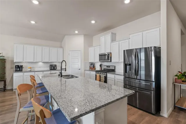 a kitchen with stainless steel appliances granite countertop a refrigerator a stove a sink a dining table and chairs