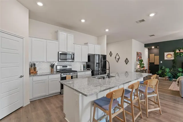 a kitchen with stainless steel appliances granite countertop a stove top oven a sink a refrigerator and white cabinets with wooden floor