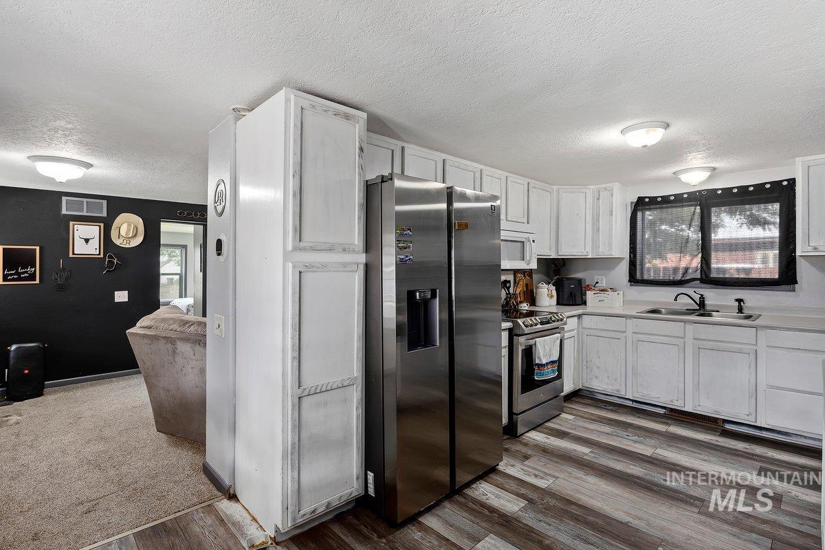 418 South Date Street Shoshone, ID 83352 - Photo 12 of 36 Kitchen featuring white cabinetry, wood-finish flooring, stainless steel appliances, and a double basin sink with a matte black faucet