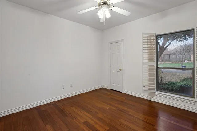 an empty room with wooden floor chandelier fan and windows