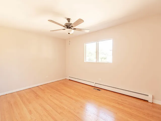 an empty room with wooden floor fan and windows