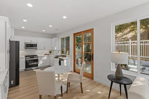 a kitchen with stainless steel appliances kitchen island granite countertop a refrigerator a stove a sink a dining table and chairs with wooden floor