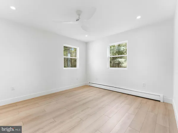 an empty room with wooden floor and way to kitchen