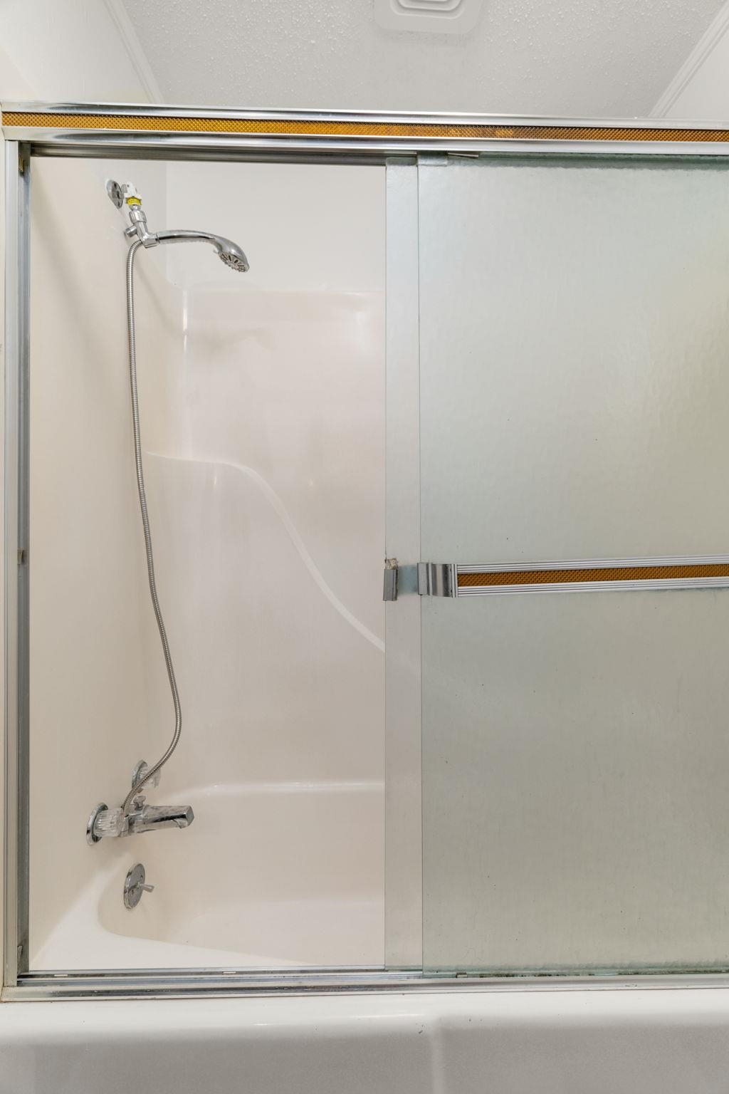 217 Red Bay Road Golden, MS 38847 - Photo 20 of 33 Bathtub with an integrated shower, featuring a sliding frosted glass enclosure and a chrome faucet