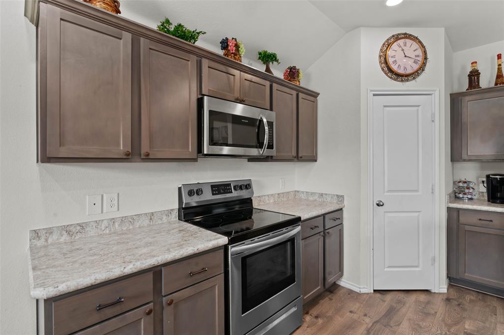 409 Wilson Way Denton, TX 76207 - Photo 3 of 33 Kitchen showcasing espresso cabinetry, light-toned countertops, a stainless steel microwave, and a black electric range