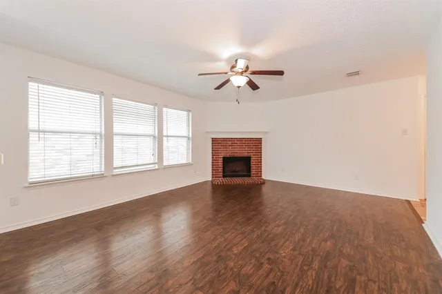 an empty room with wooden floor chandelier fan and windows