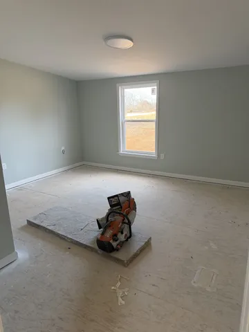 a view of a hallway to an empty room with wooden floor and a window
