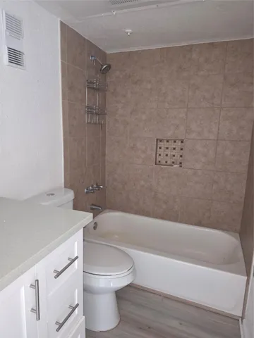 a bathroom with a granite countertop bathtub shower sink vanity and toilet